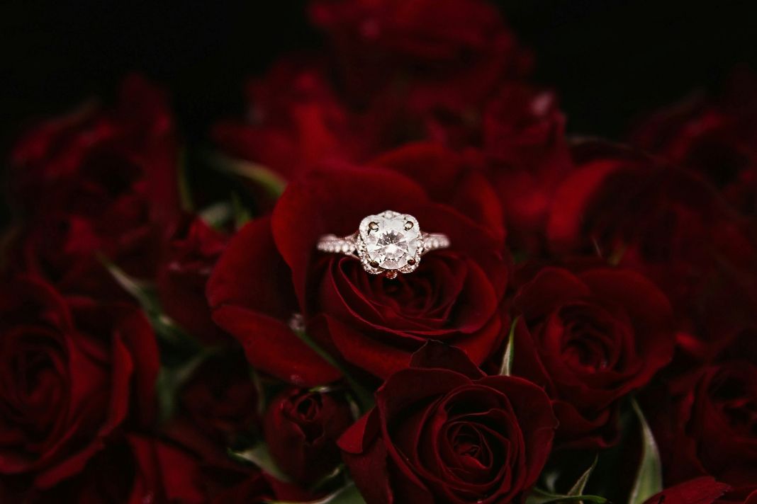 a diamond ring nested in a rose that is in a bed of roses