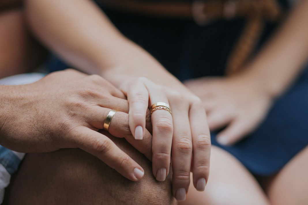 a close up photo of a couple holding hands wearing their wedding rings